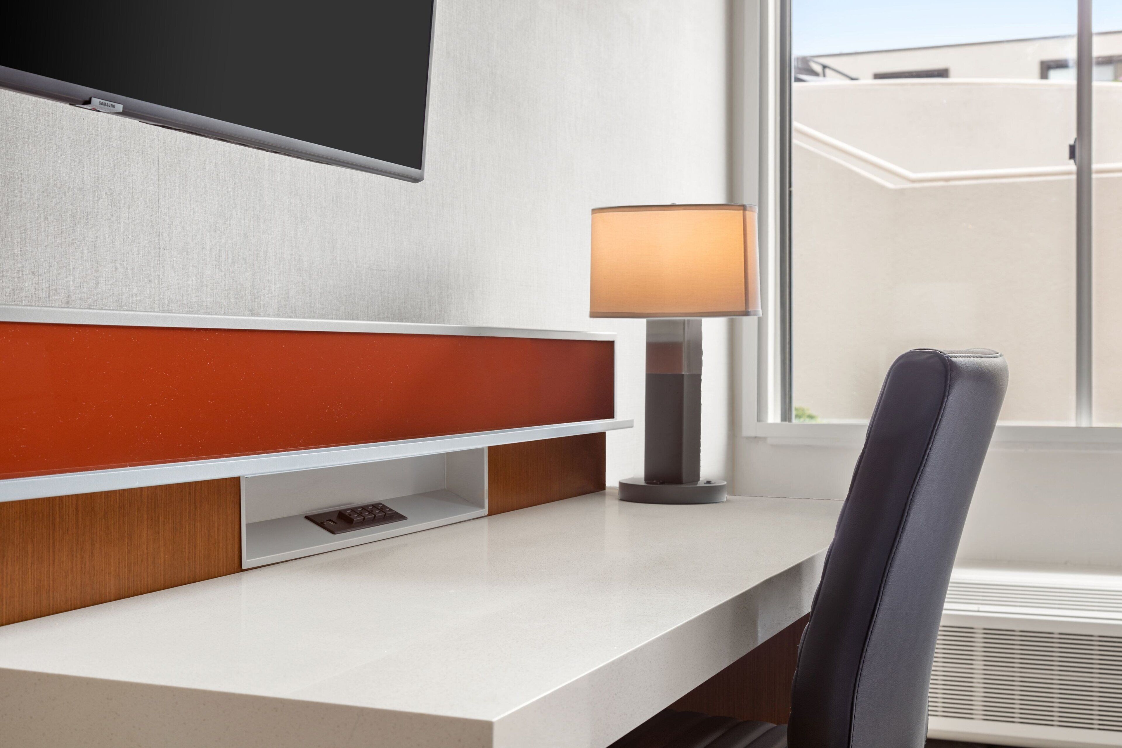 Ein modernes Hotelzimmer mit einem an der Wand befestigten Flachbildfernseher, einem Schreibtisch mit Lampe und einem Sessel.
