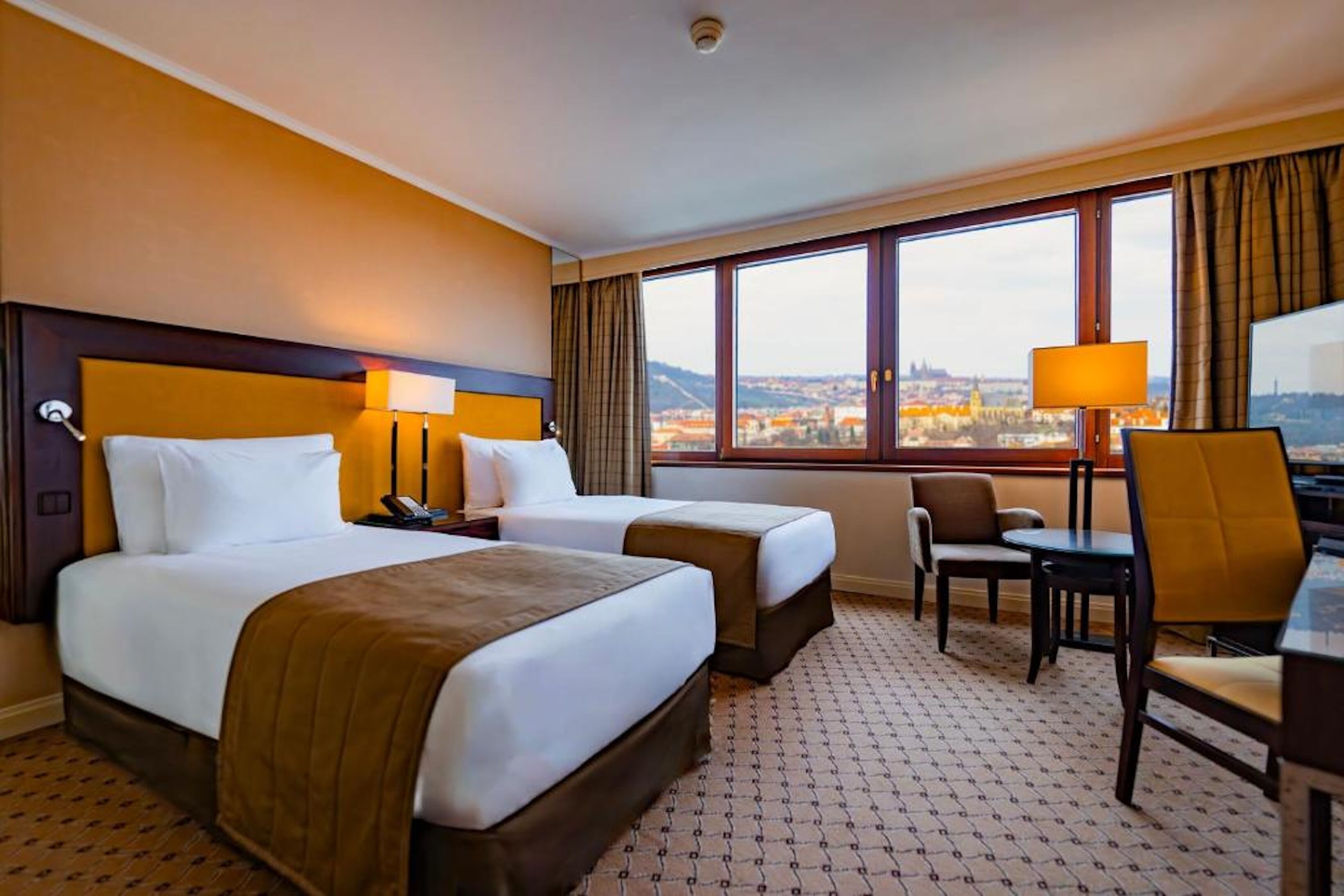 Habitación de hotel con dos camas, un escritorio, una silla y vistas a la ciudad.