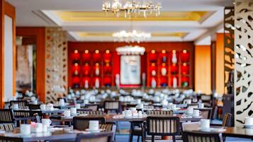 A spacious restaurant with multiple tables and chairs, a chandelier, and a red decorative wall in the background.
