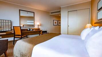 A hotel room with a large bed, a desk, a chair, a mirror, and framed pictures on the wall.