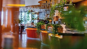 A restaurant interior with a curved counter, hanging lights, and potted plants. - Grand Hotel Prague Towers (Prague)