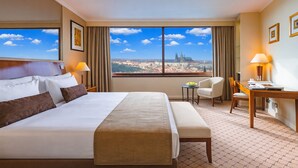 A hotel room with a large bed, a desk, a chair, and a view of a cityscape. - Grand Hotel Prague Towers (Prague)