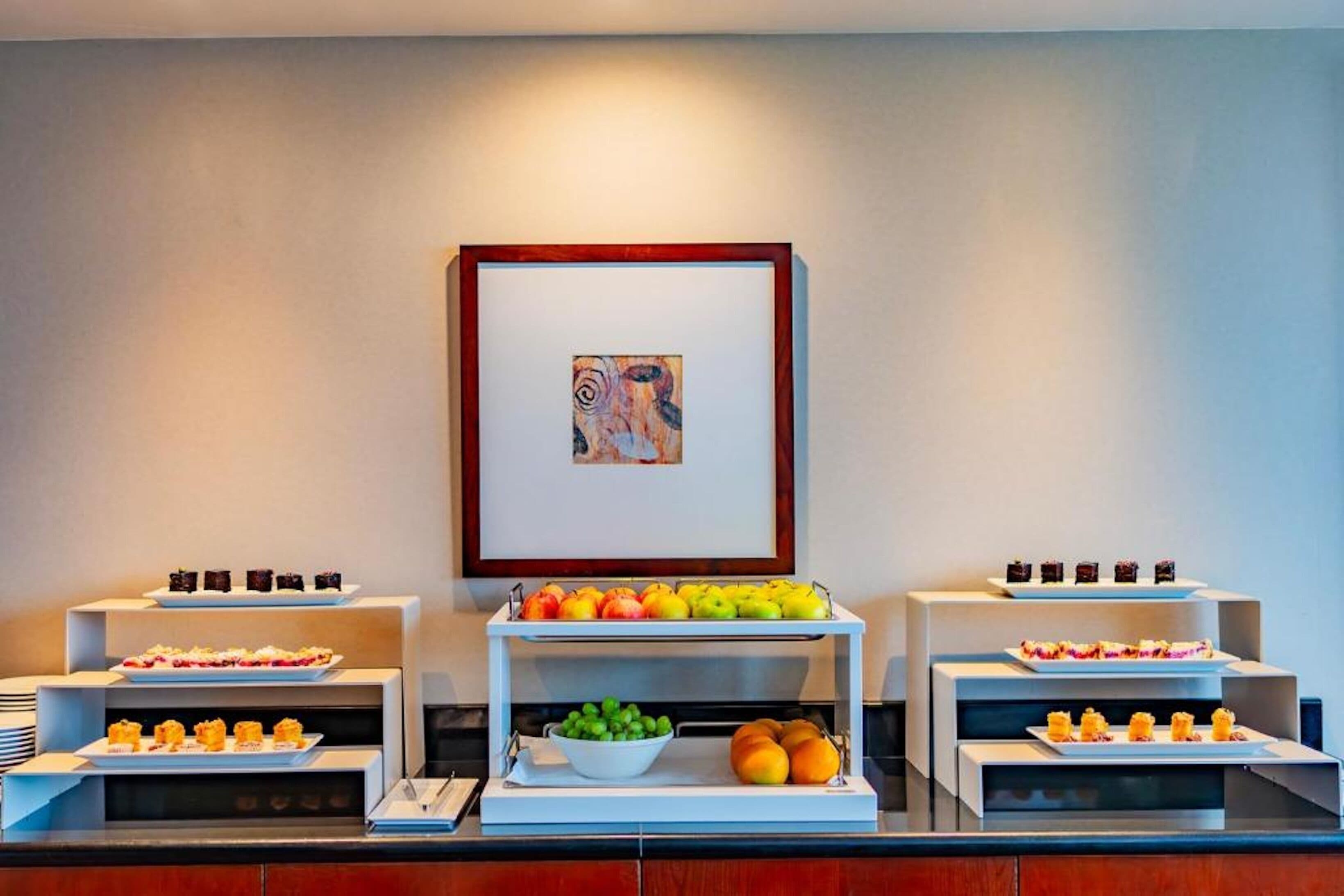 Montaje de bufé con diferentes alimentos y una obra de arte enmarcada en la pared.