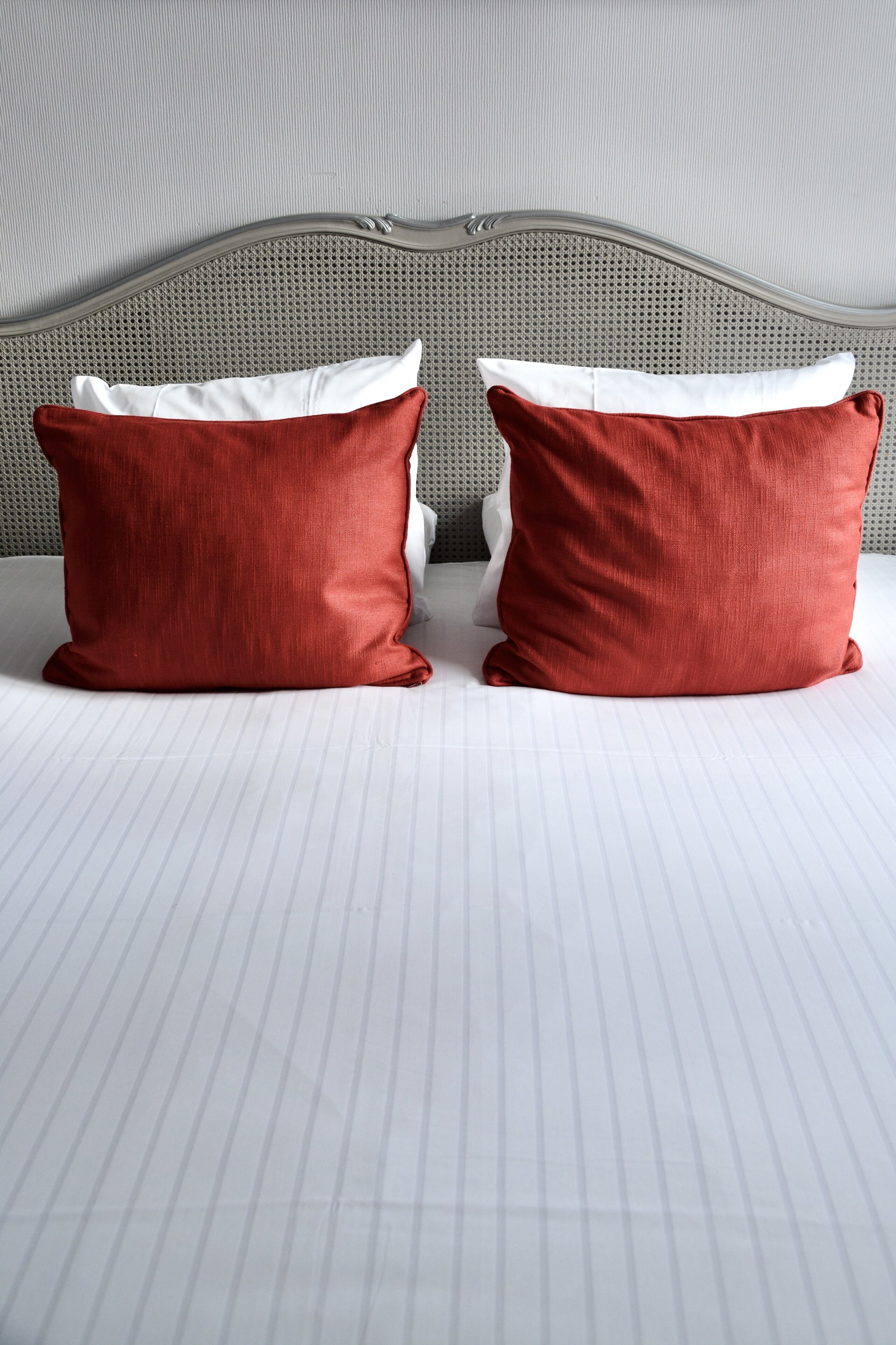 Una cama con cabecera gris tapizada y dos almohadas rojas.
