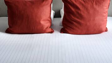 Una cama con cabecera gris tapizada y dos almohadas rojas.