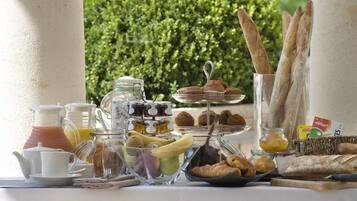 Un buffet de petit-déjeuner proposant une variété d’aliments et de boissons, notamment des viennoiseries, du pain et des fruits, le tout dans un cadre verdoyant.