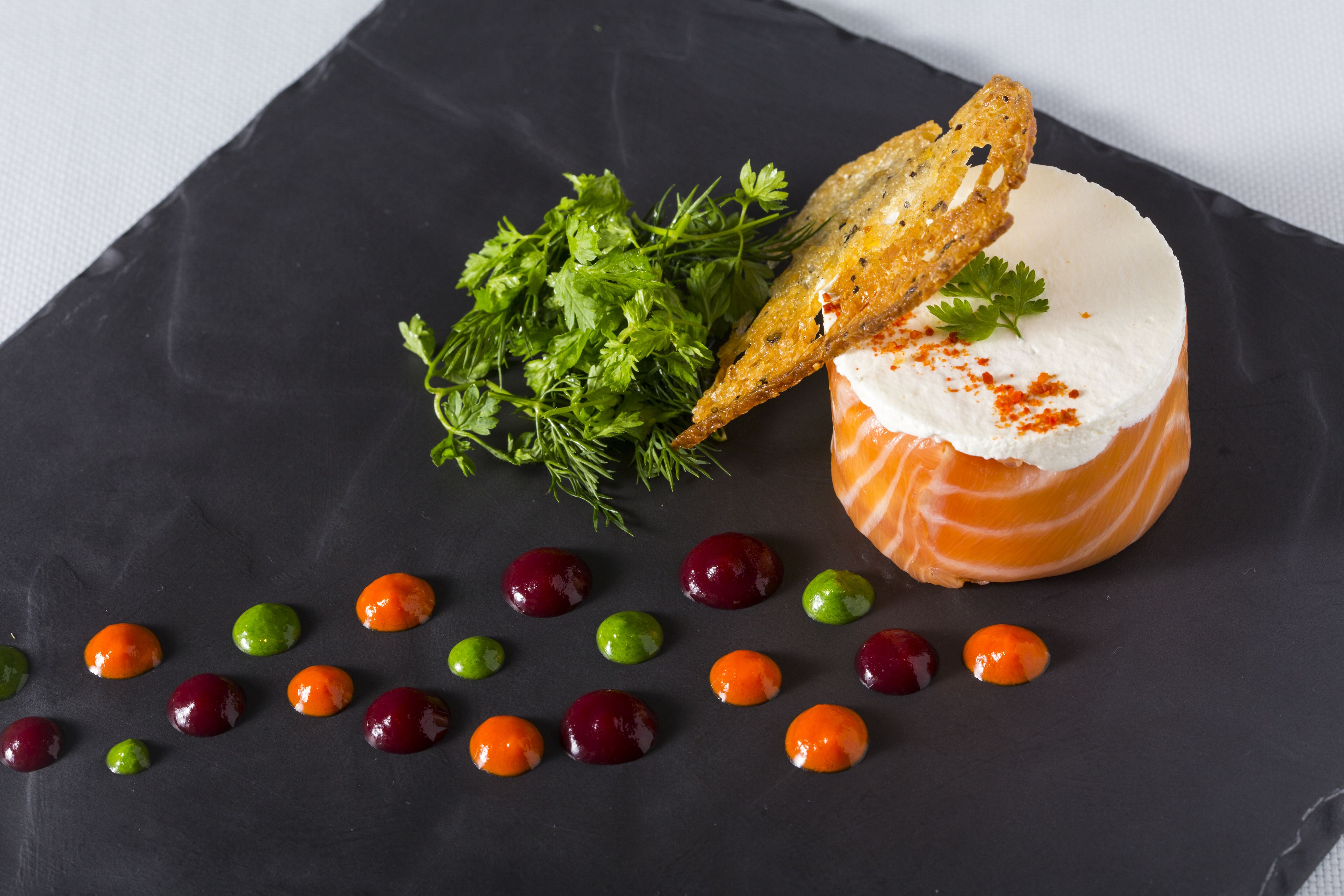 Ein Gericht mit Lachs, Brot und Garnitur auf einer dunklen Schieferplatte.
