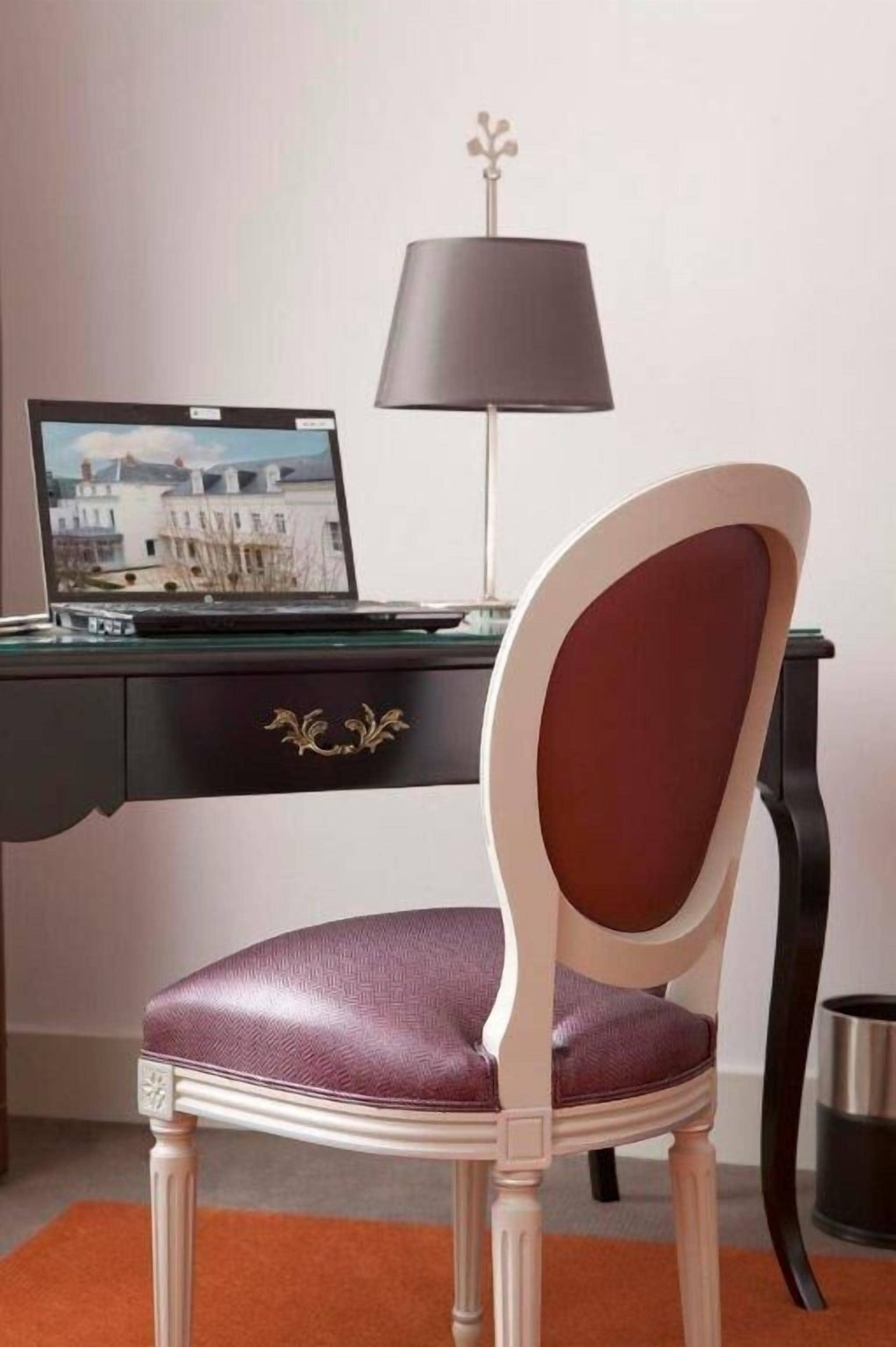Una habitación con un escritorio, una silla, una lámpara y una computadora portátil mostrando un paisaje urbano.