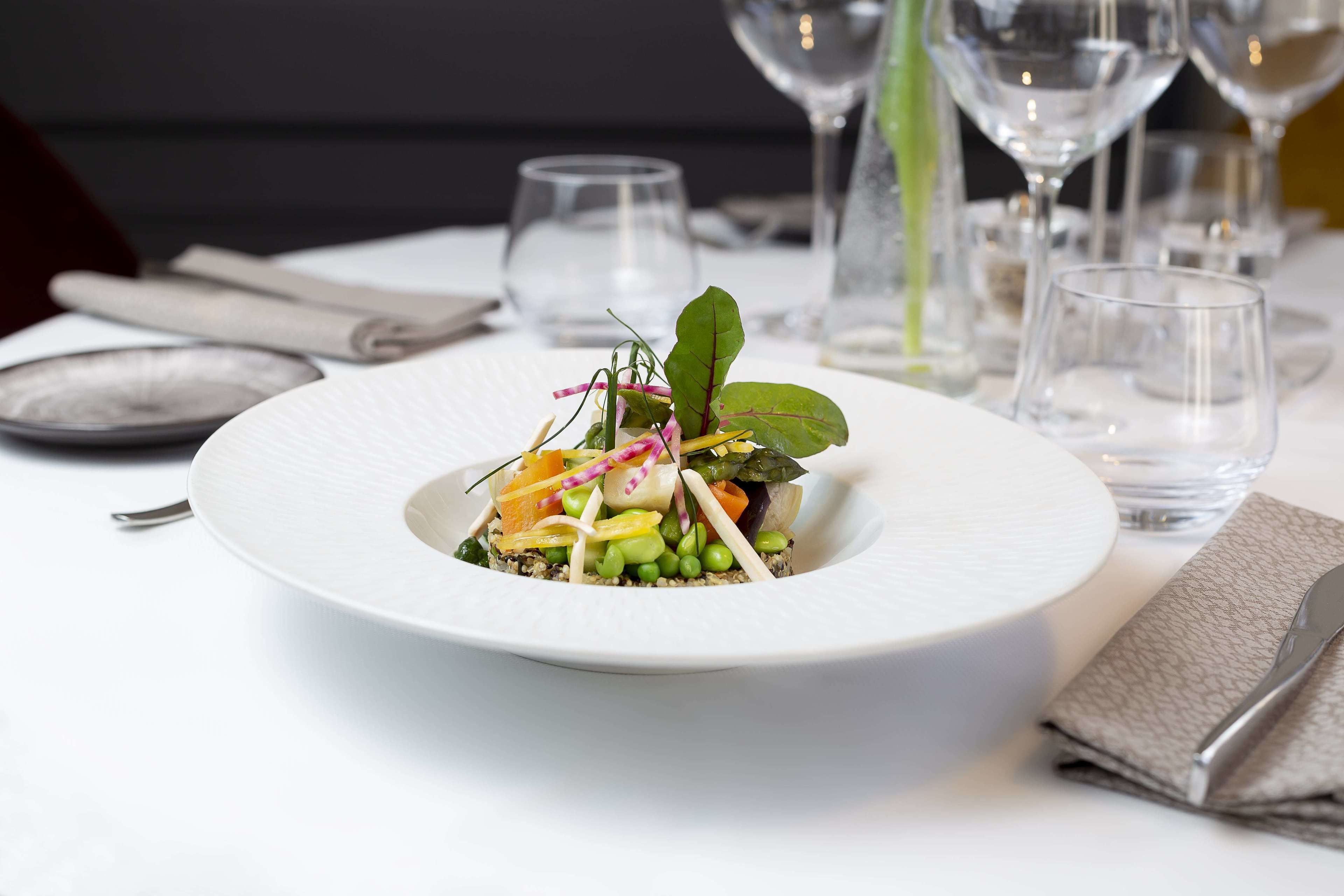 Un plato blanco con ensalada sobre una mesa, rodeado de copas de vino vacías y una servilleta.
