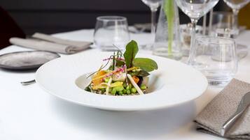 Un plato blanco con ensalada sobre una mesa, rodeado de copas de vino vacías y una servilleta.