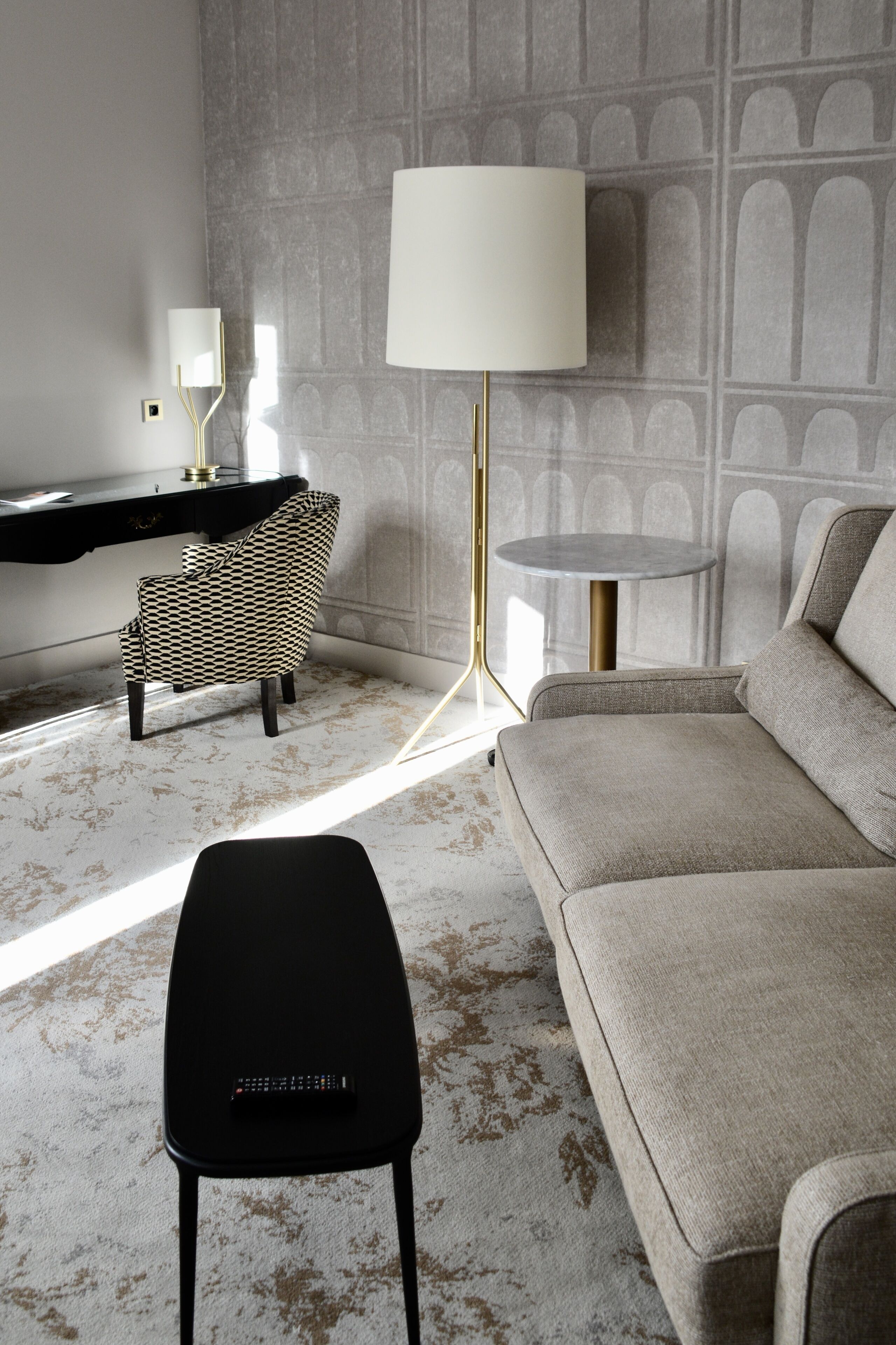 Una sala de estar moderna con un sofá, un sillón estampado, una mesita y una lámpara de pie.