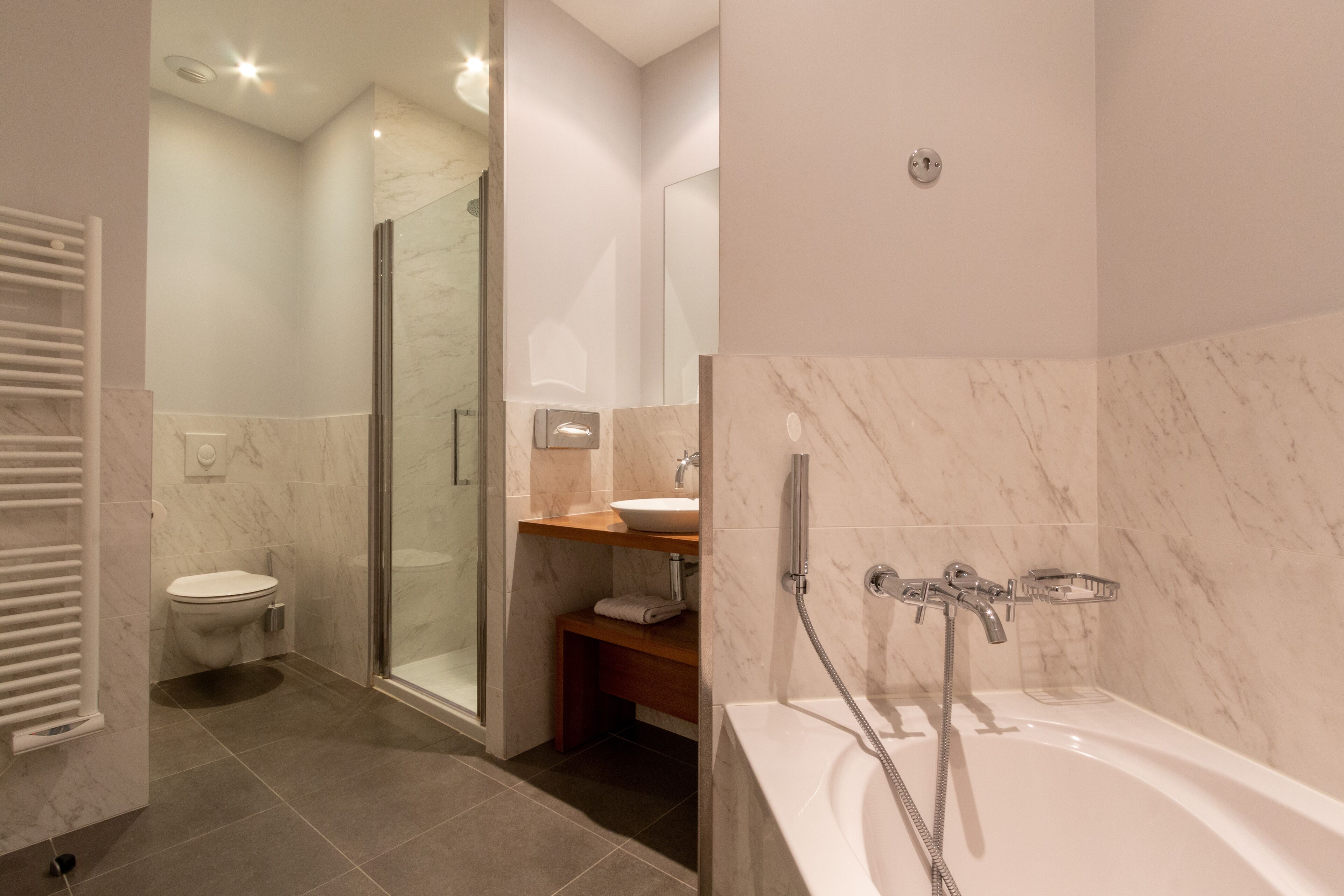 Ein modernes Badezimmer mit Duschkabine aus Glas, einer weißen Badewanne und einem hölzernen Waschtisch.