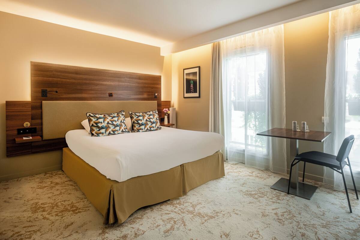 Une chambre d’hôtel avec un grand lit, un bureau avec une chaise et une fenêtre avec des rideaux.