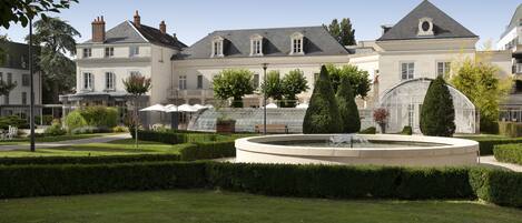 A large building with a formal garden, including a fountain and trimmed hedges.