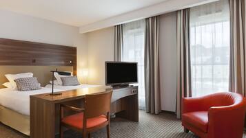 A hotel room with a bed, desk, TV, and red chair.