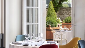 An indoor dining area with a table set for a meal, chairs in various colors, and a view of the outdoor garden through an open door. - Château Belmont Tours by The Crest Collection (Tours)
