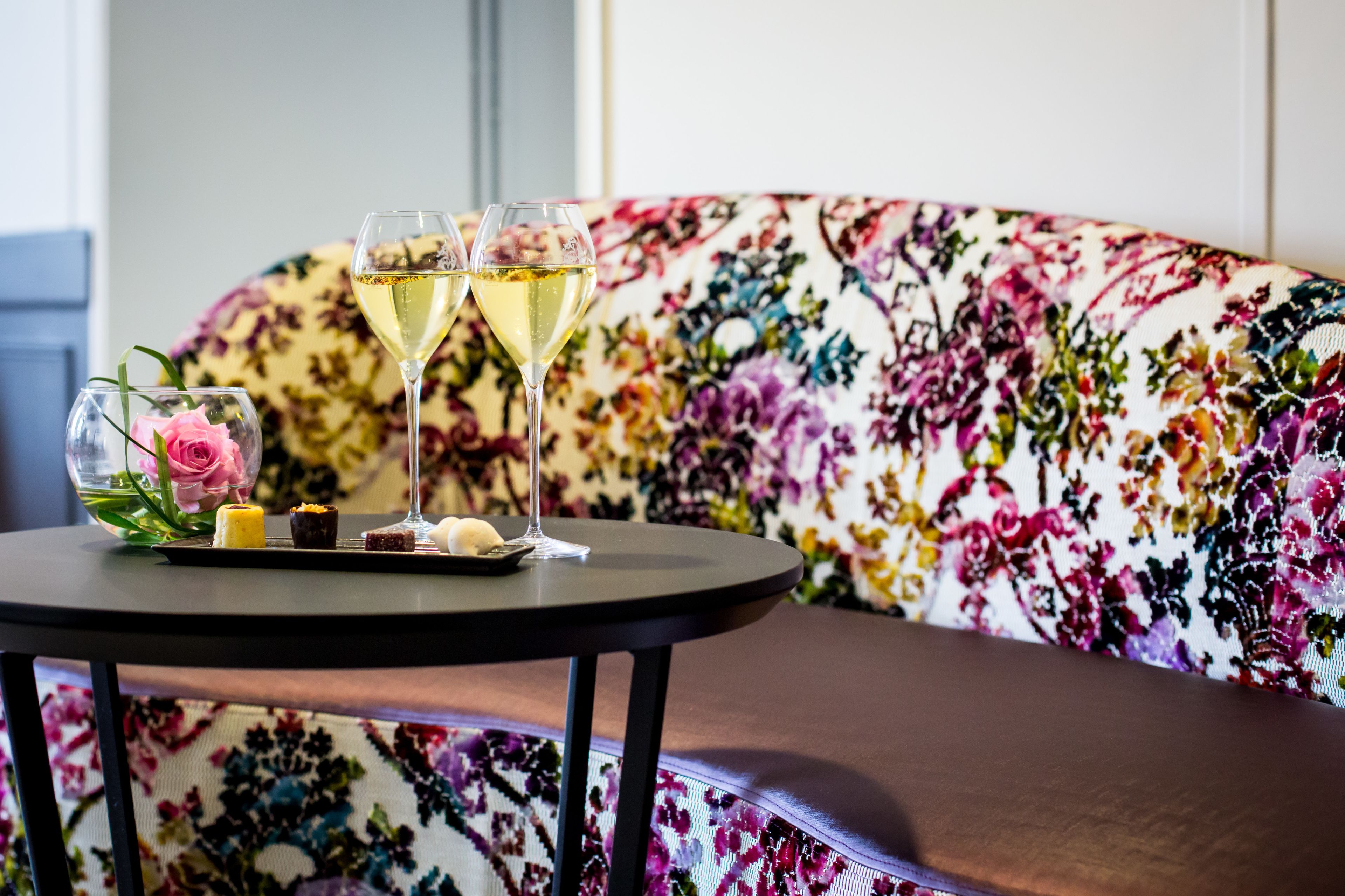 Une table ronde avec deux verres de vin blanc, une rose rose et de petits desserts.