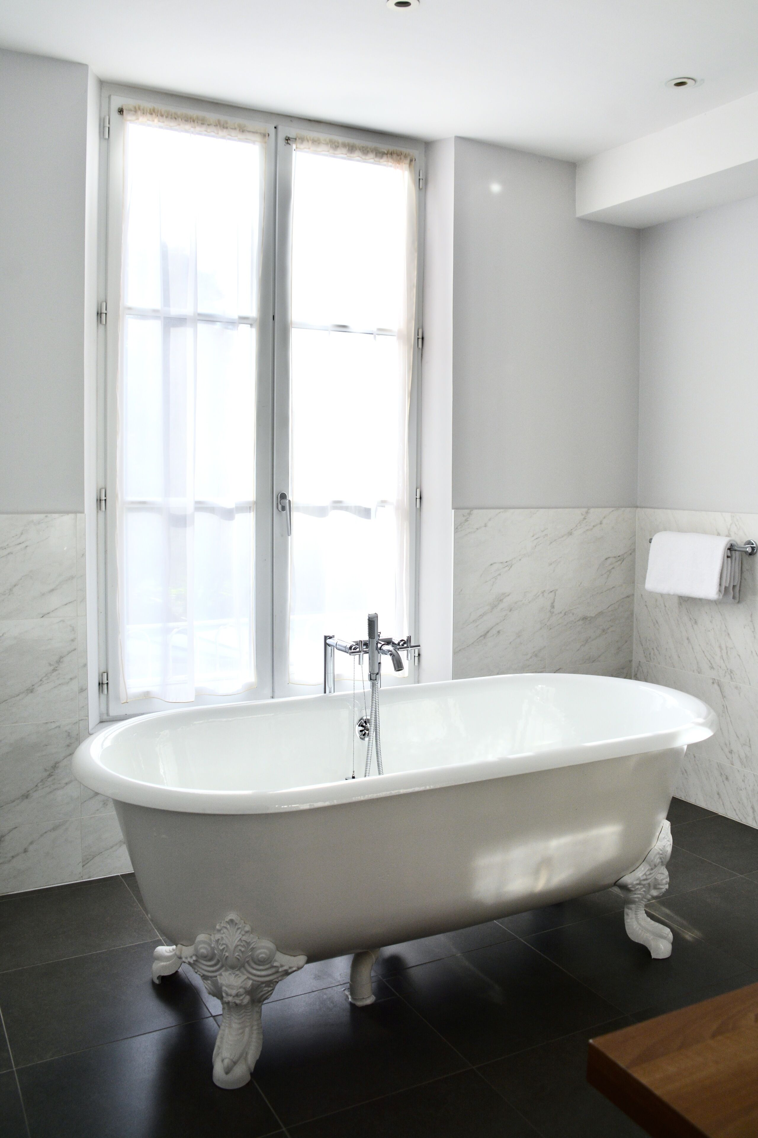 A modern bathroom with a freestanding bathtub, large windows, and marble walls.
