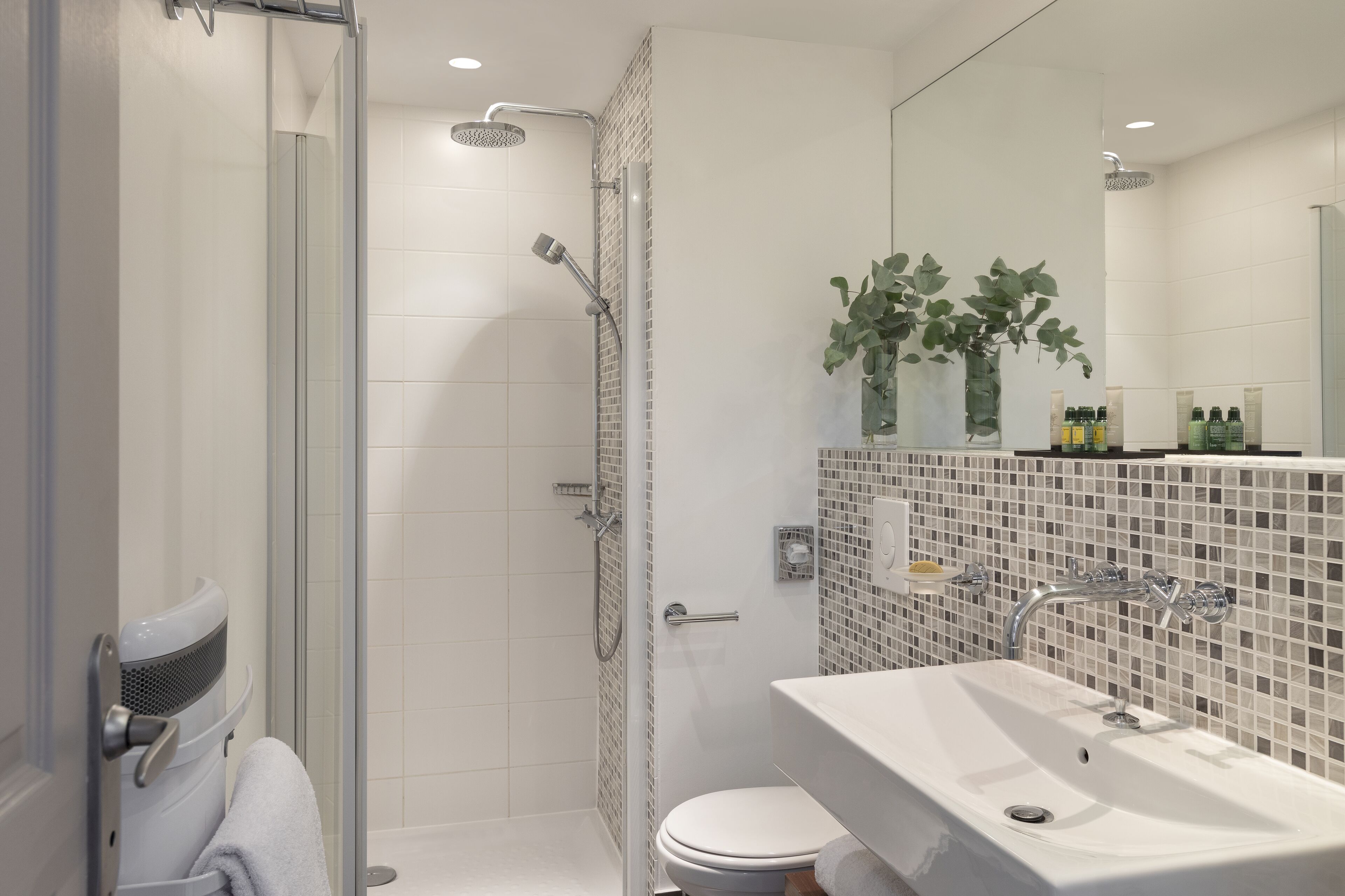 Een moderne badkamer met een douchecabine van glas, een wit wastafelmeubel en een spiegel met toiletartikelen.