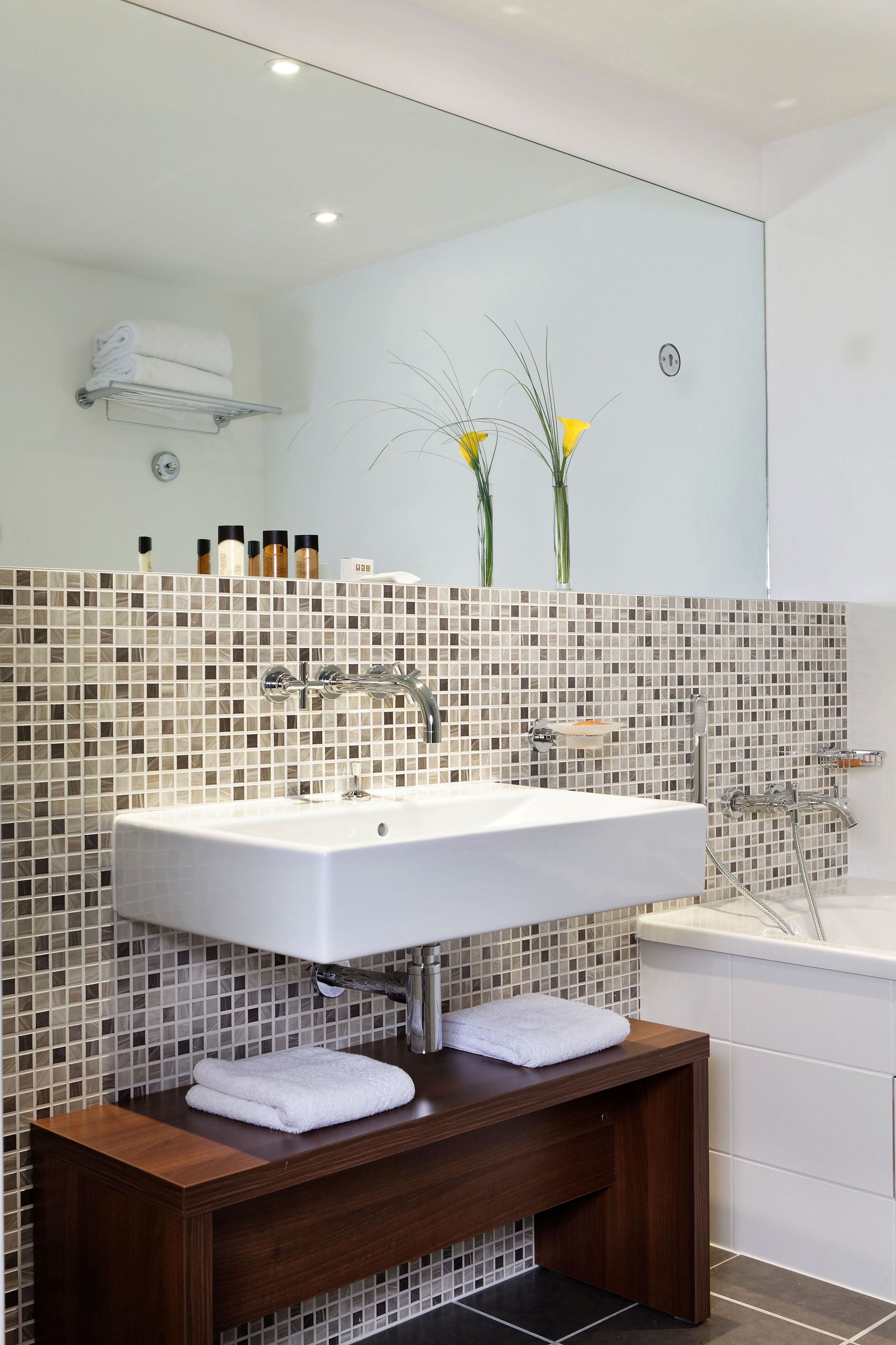 A modern bathroom with a large white sink, a wooden vanity, and a glass shower enclosure.