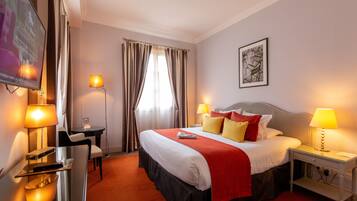 Habitación de hotel con cama, lámparas de noche, escritorio con lámpara, televisor y ventana con cortinas.