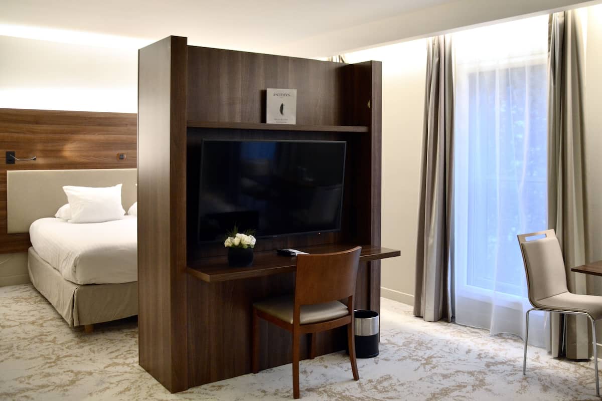 Une chambre d’hôtel avec un lit, un bureau avec une télévision, une chaise et une fenêtre avec des rideaux.