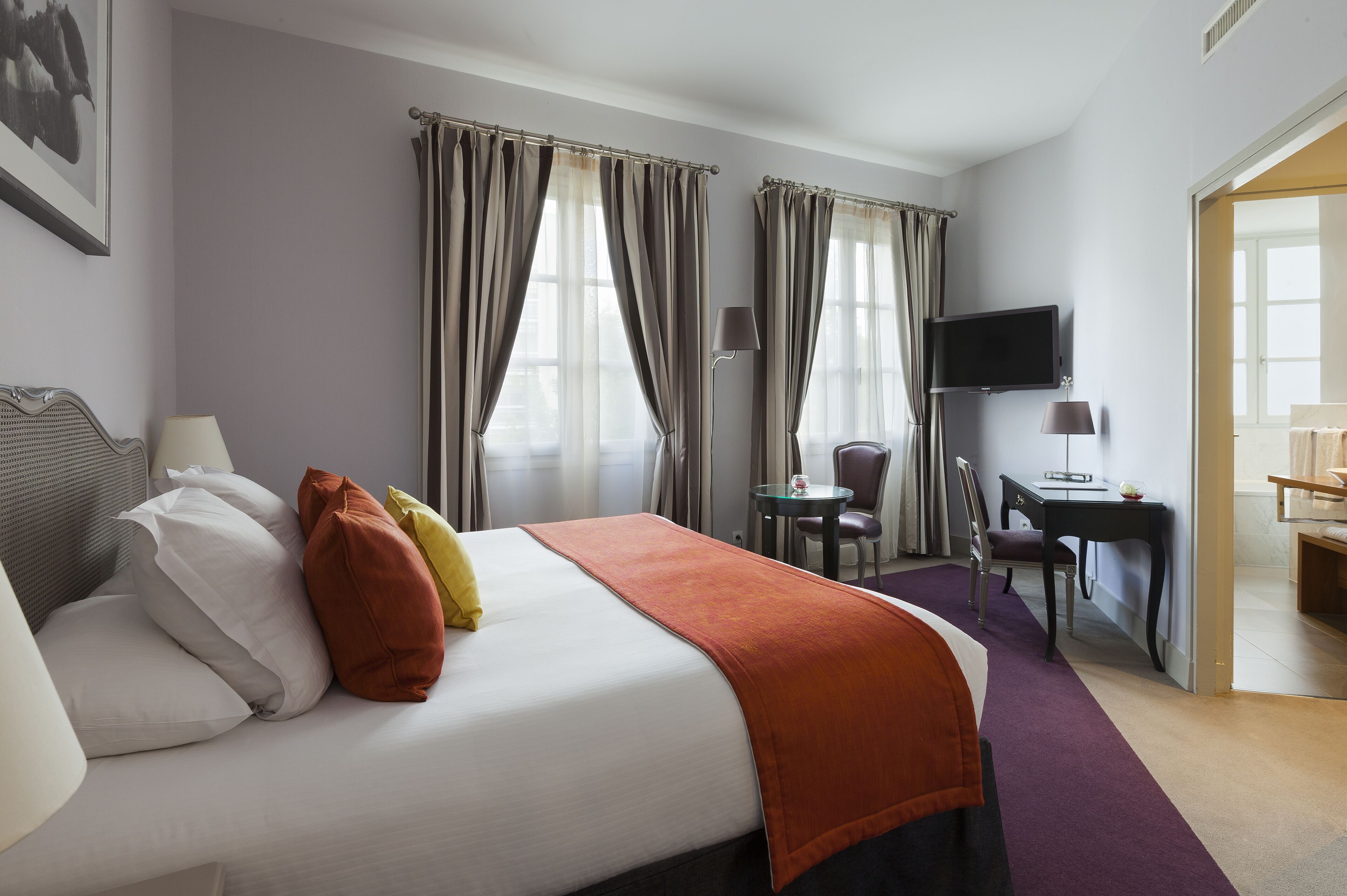 A hotel room with a bed, a desk, a chair, a TV, and curtains.