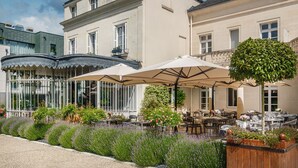 An outdoor seating area with tables and chairs, surrounded by plants and a decorative fence. - Château Belmont Tours by The Crest Collection (Tours)