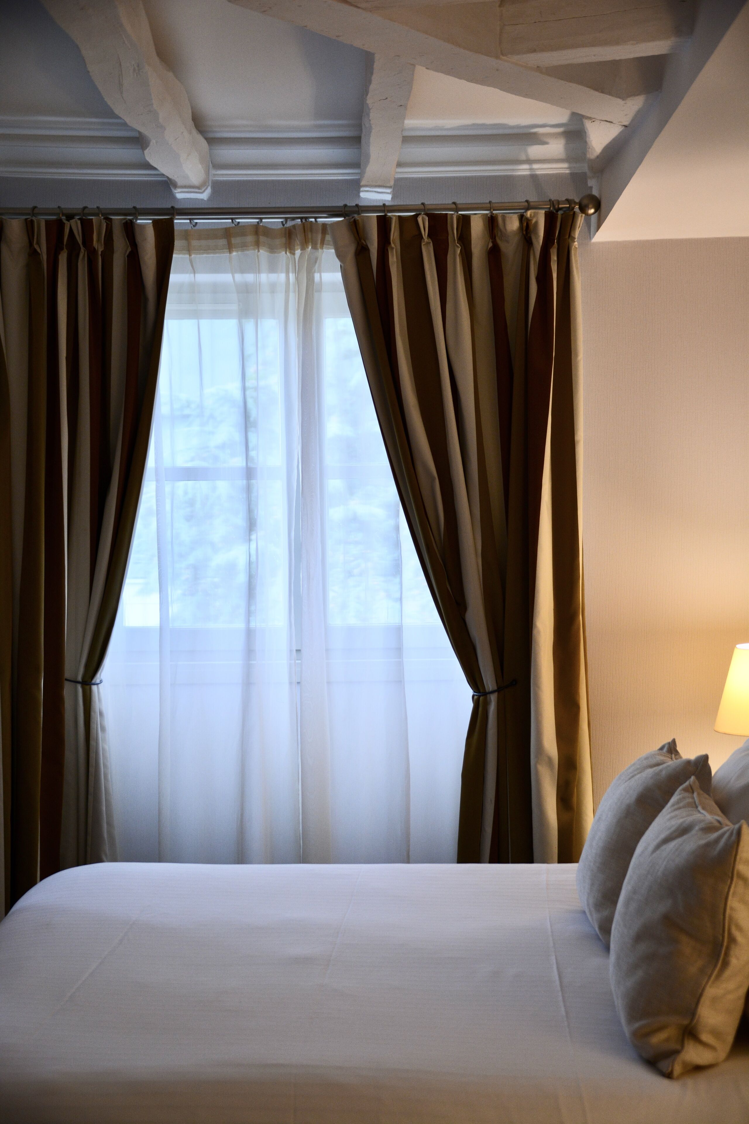 A hotel room with a large bed, beige curtains, and a window with a view of trees.