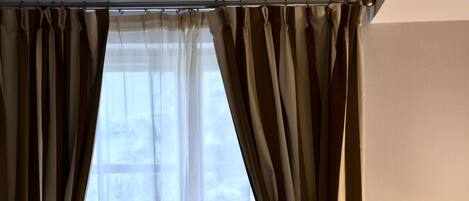 Une chambre d’hôtel avec un grand lit, des rideaux de couleur beige et une fenêtre donnant sur des arbres.