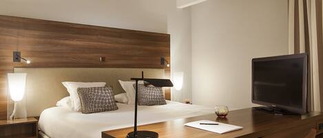 A hotel room with a bed, bedside lamps, a desk with a television, and a chair.