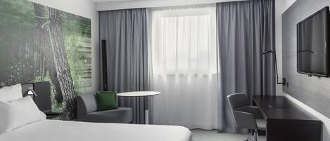 A modern hotel room with a large bed, a desk, a chair, and a TV mounted on the wall.