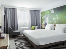 Habitación de hotel con cama, escritorio, silla, mesita y pared verde con diseño floral.