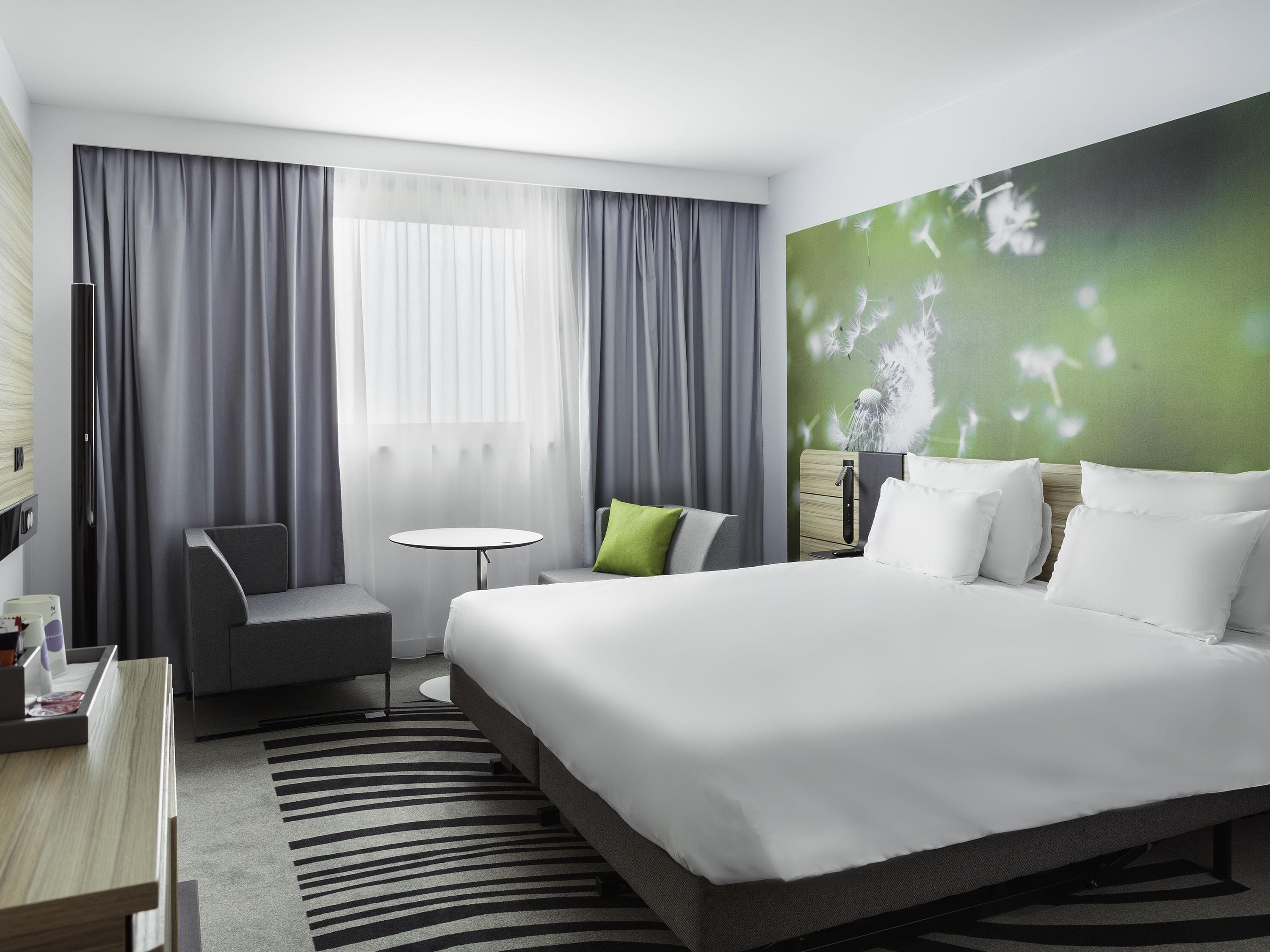 A modern hotel room with a large bed, a small round table, a chair, and a desk with a computer.