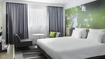 A modern hotel room with a large bed, a small round table, a chair, and a desk with a computer.