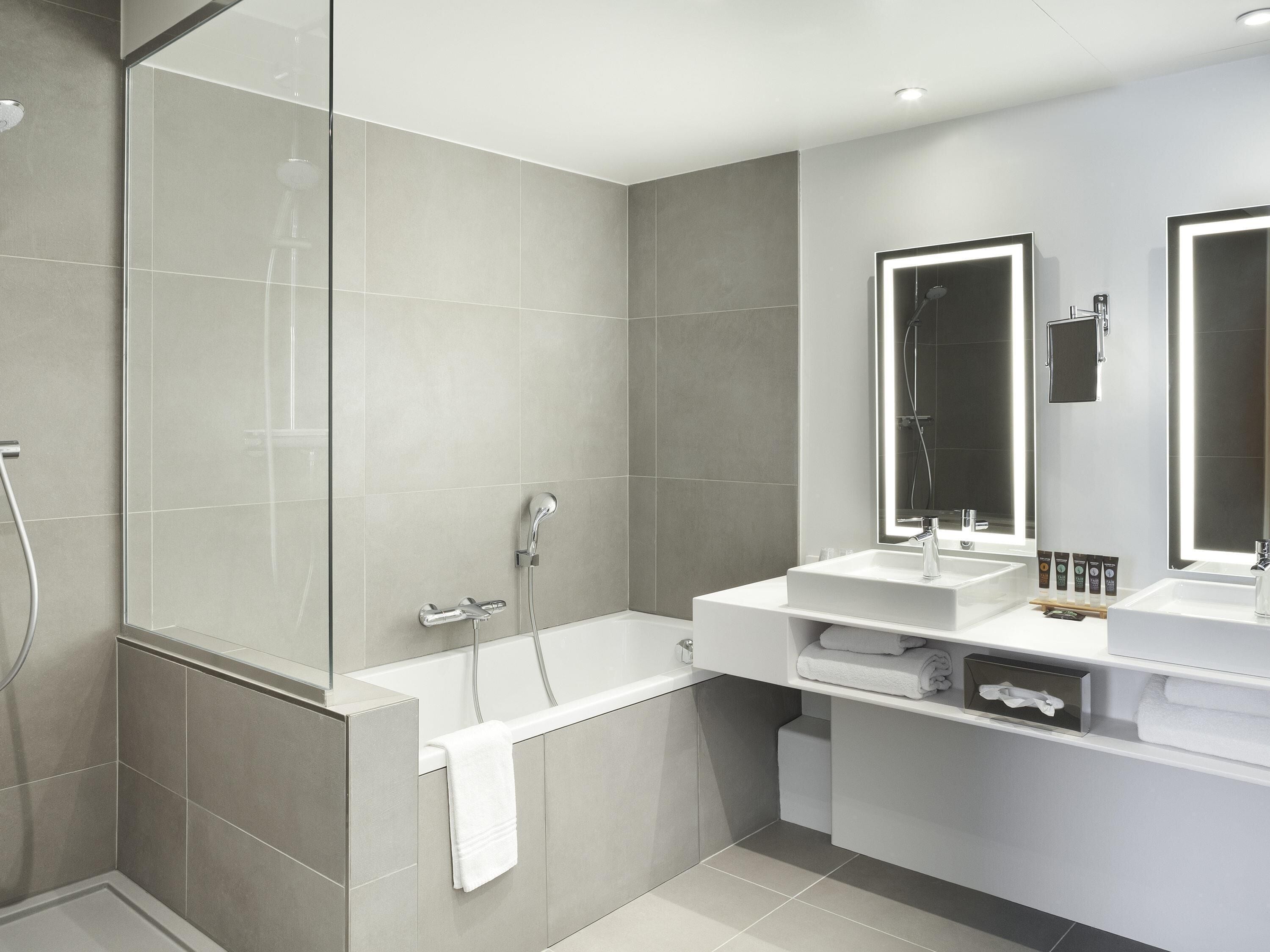 Un baño moderno con ducha acristalada, bañera y dos lavamanos con espejos.
