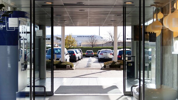 A hotel entrance with a view of parked cars and a mountain in the background. - Novotel Paris Charles de Gaulle Airport (Tremblay-en-France)