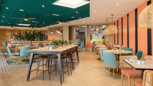 A modern restaurant with high ceilings, wooden floors, and a variety of seating arrangements including tables and chairs. - Novotel Paris Charles de Gaulle Airport (Tremblay-en-France)