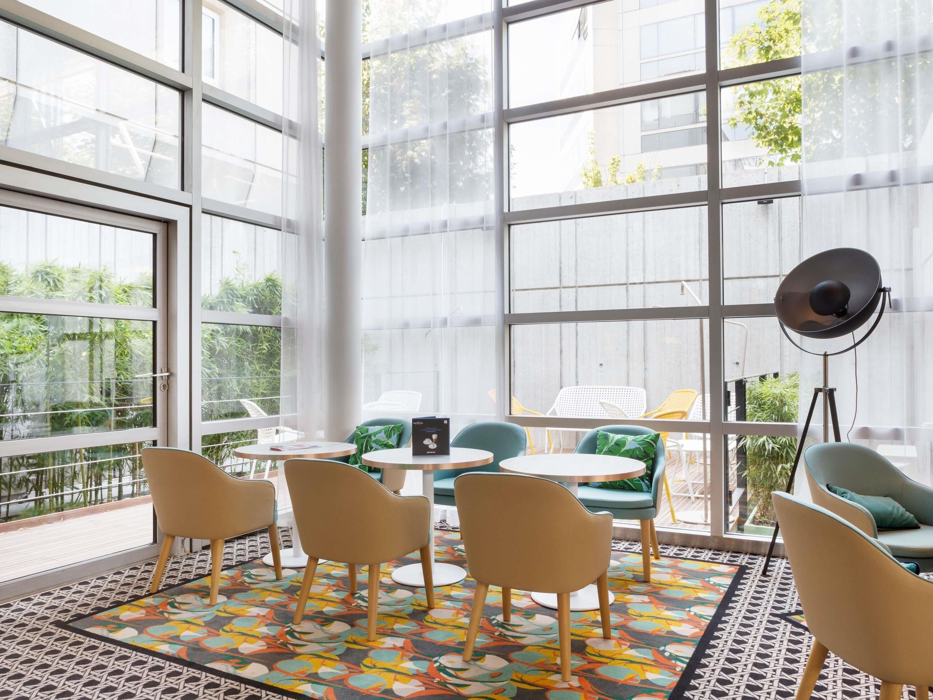 A spacious indoor area with large windows, round tables, and chairs.