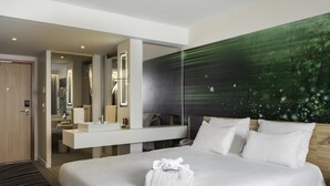 A modern hotel room with a large bed, a built-in desk, a large mirror, and a green abstract wall. - Novotel Paris Charles de Gaulle Airport (Tremblay-en-France)