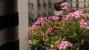 A view of a building with multiple windows and balconies, surrounded by other buildings and pink flowers in the foreground. - Relais Saint Germain (Paris)
