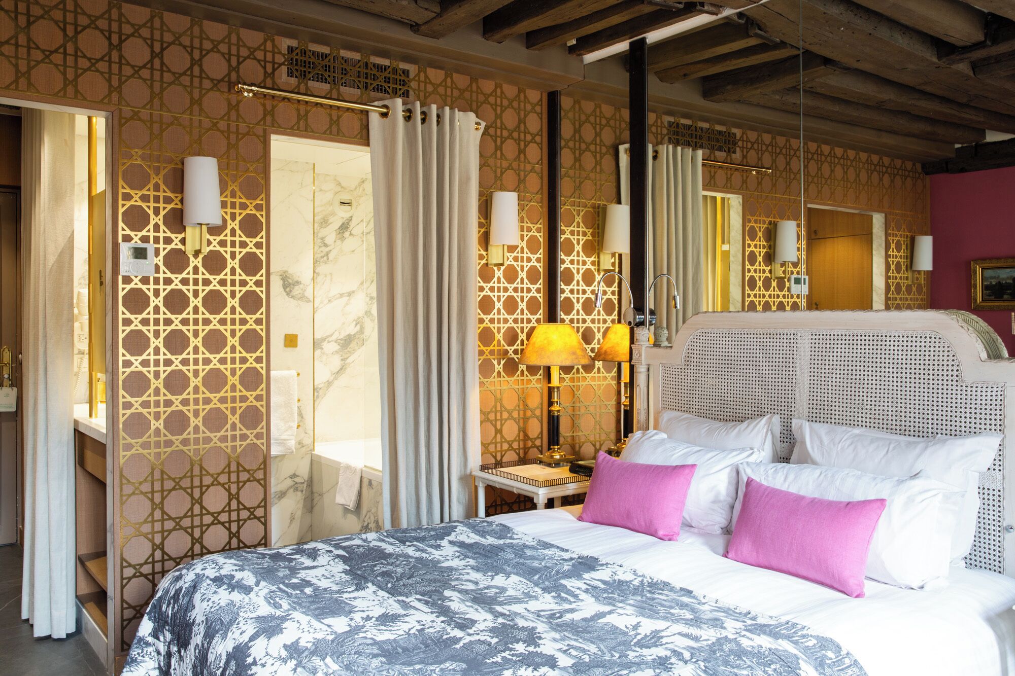 Habitación de hotel con una cama grande, una mesita de noche con lámpara y un baño visible a través de una puerta abierta.