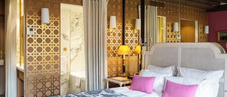 Habitación de hotel con una cama grande, una mesita de noche con lámpara y un baño visible a través de una puerta abierta.