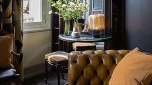A corner room with a dark brown leather sofa, a small round table with a vase of flowers, a mirror, and a bookshelf. - Relais Saint Germain (Paris)