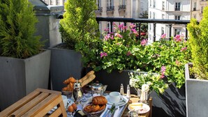 A rooftop terrace with a dining table set for breakfast, surrounded by potted plants and flowers. - Relais Saint Germain (Paris)