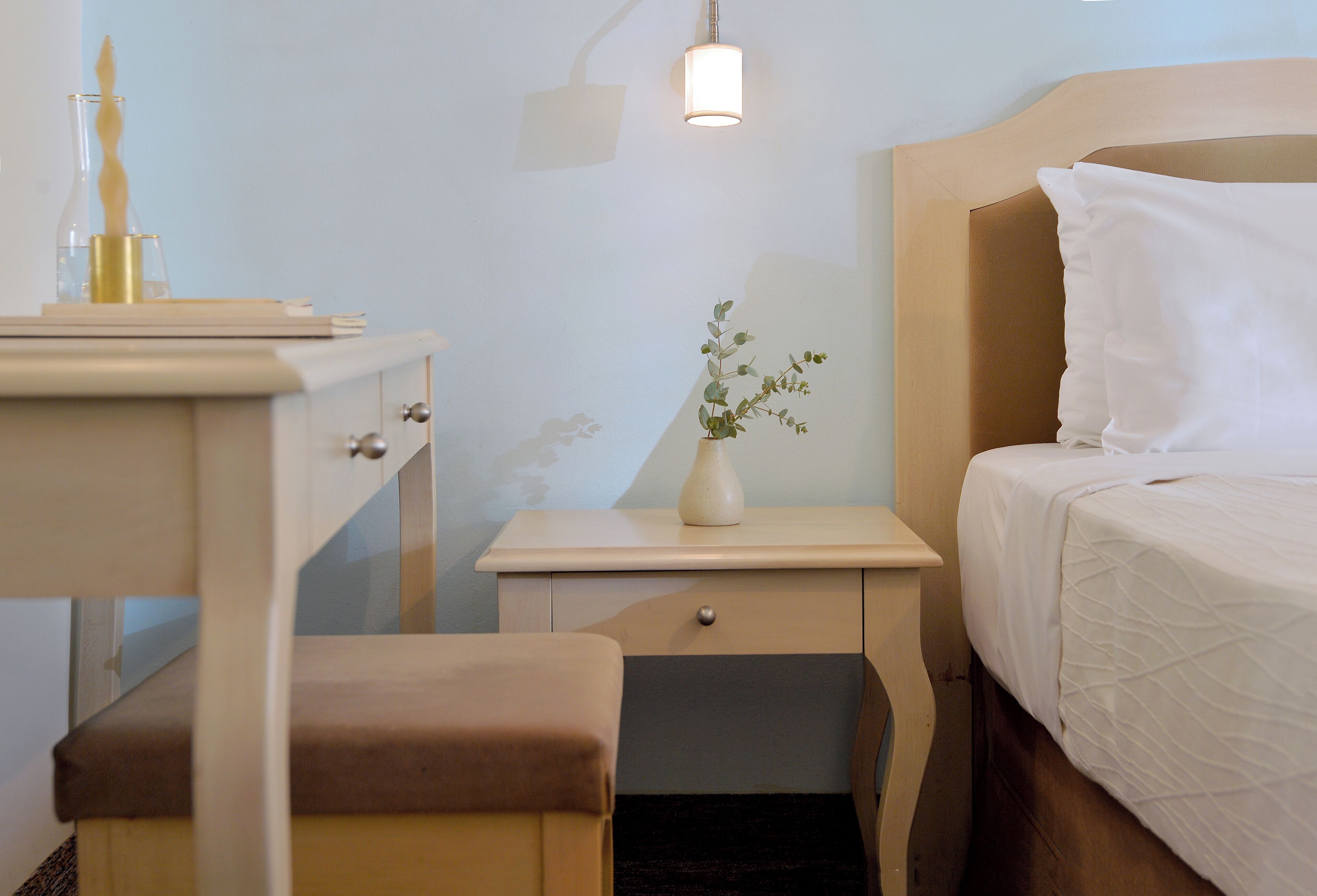 Ein Hotelzimmer mit Bett, Nachttisch, Hocker und einer Pflanze in einer Vase.