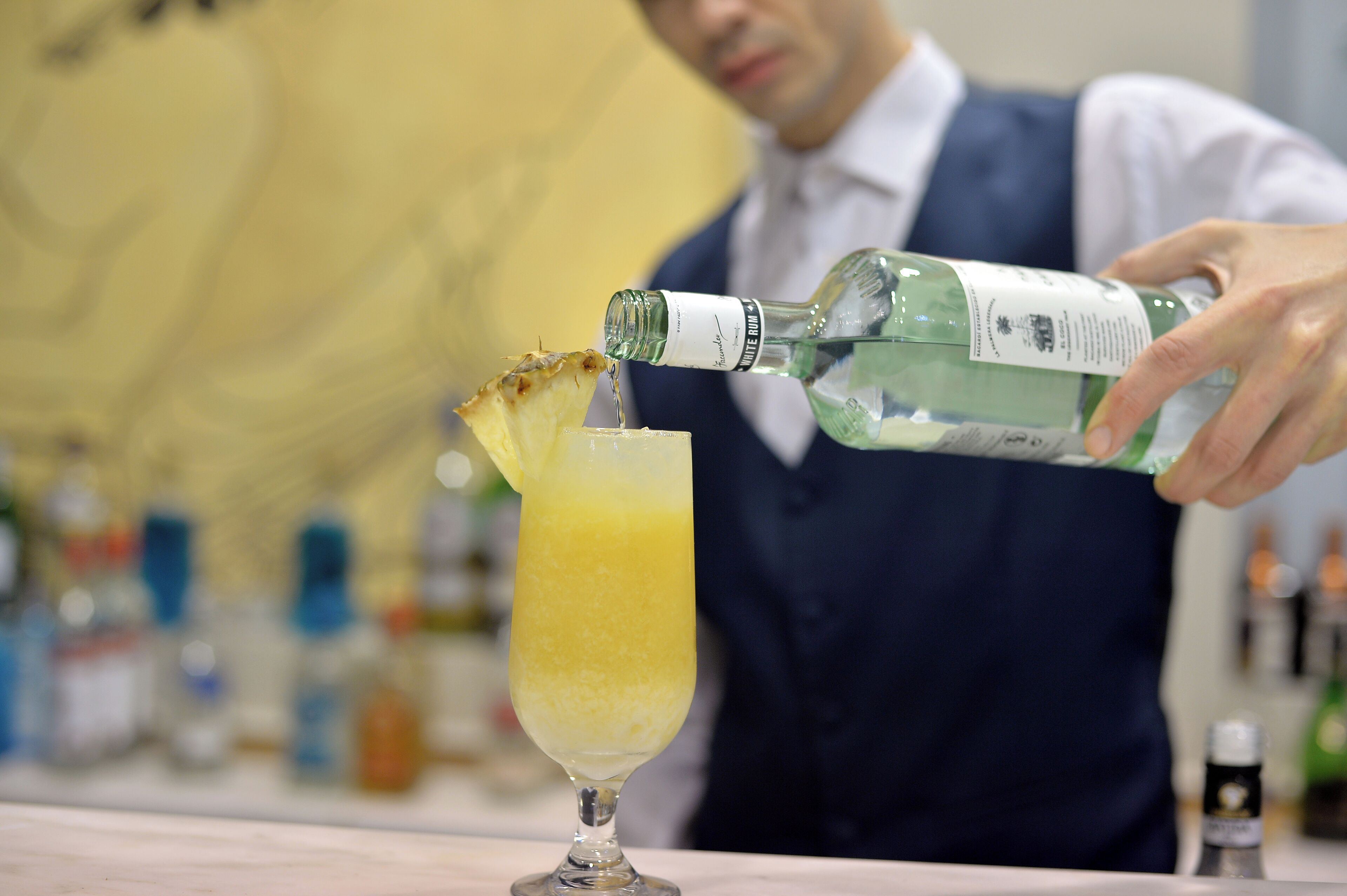 Ein Barkeeper gießt ein Getränk in ein Glas mit Ananas-Garnitur ein.