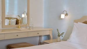 Habitación de hotel con una cama, una mesita de noche con un florero y una lámpara, un aparador con cajones y un espejo grande.