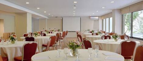A conference room with multiple round tables, each set with chairs, documents, and floral centerpieces.