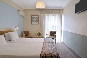 A hotel room with two beds, a desk, a chair, a TV, and a window with curtains.